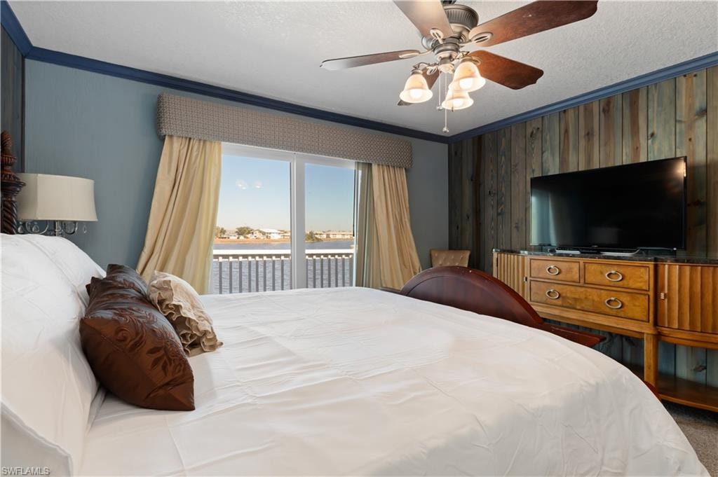 Bedroom with access to exterior, a textured ceiling, ornamental molding, a ceiling fan, and wooden walls