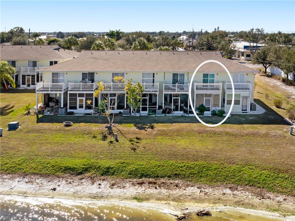 Rear view of property featuring a patio, a yard, a shingled roof, and a balcony