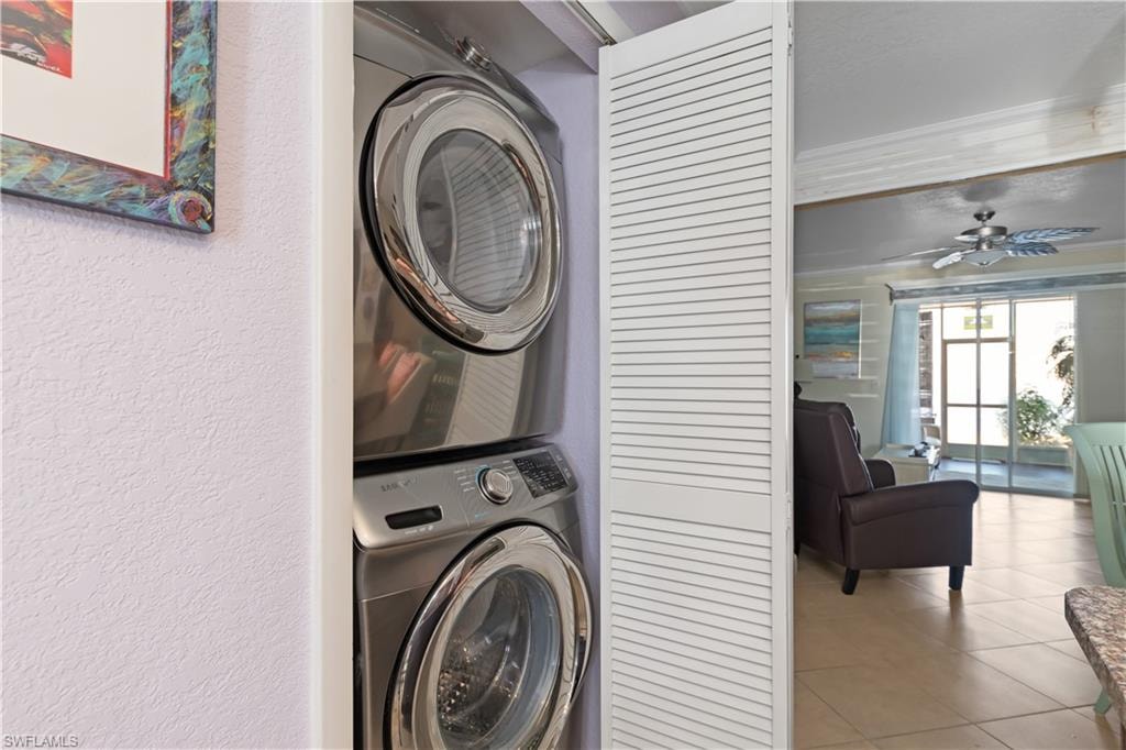 Laundry area featuring stacked washer and clothes dryer, light tile patterned floors, and a ceiling fan