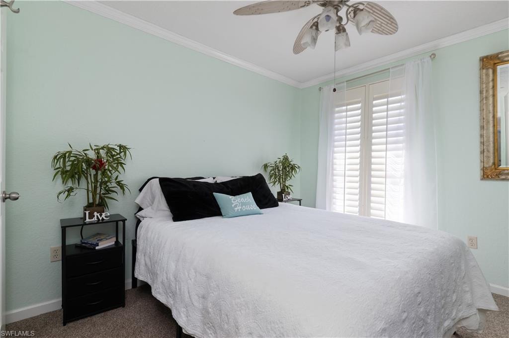 Bedroom featuring dark carpet, crown molding, and ceiling fan