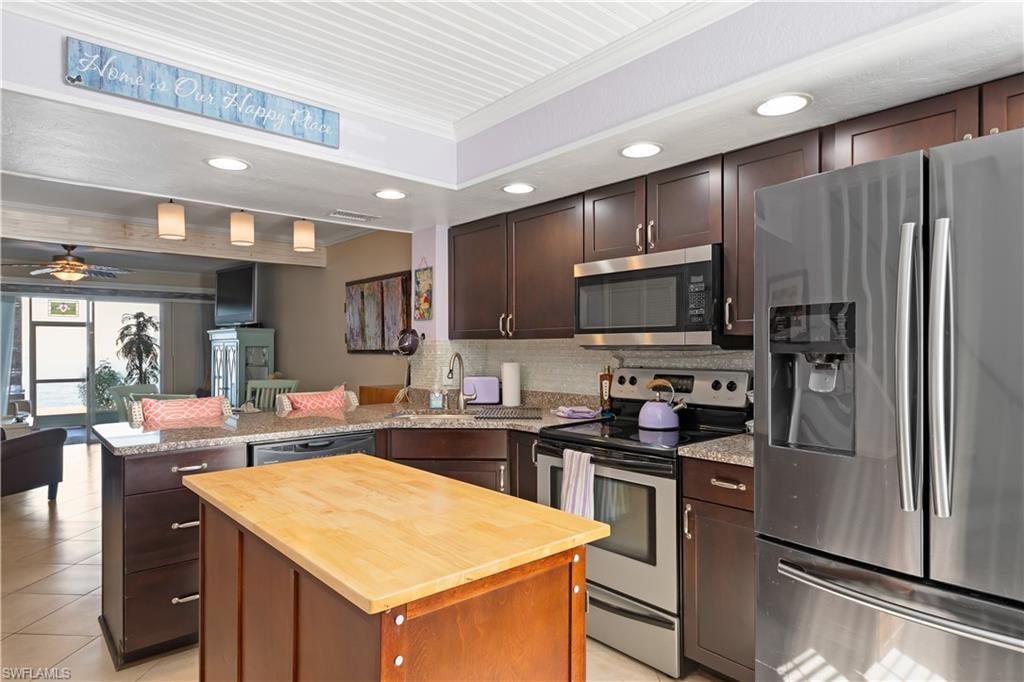 Kitchen with wooden counters, stainless steel appliances, dark wood finish cabinets, ornamental molding, and recessed lighting