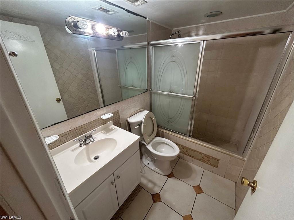 Bathroom with vanity, tiled shower, tile walls, and tile patterned flooring