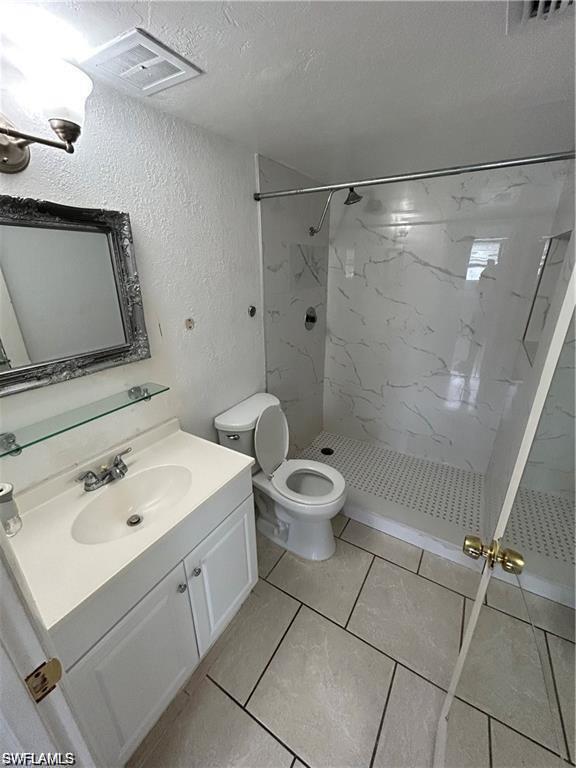 Bathroom featuring a marble finish shower, vanity, a textured wall, and a textured ceiling