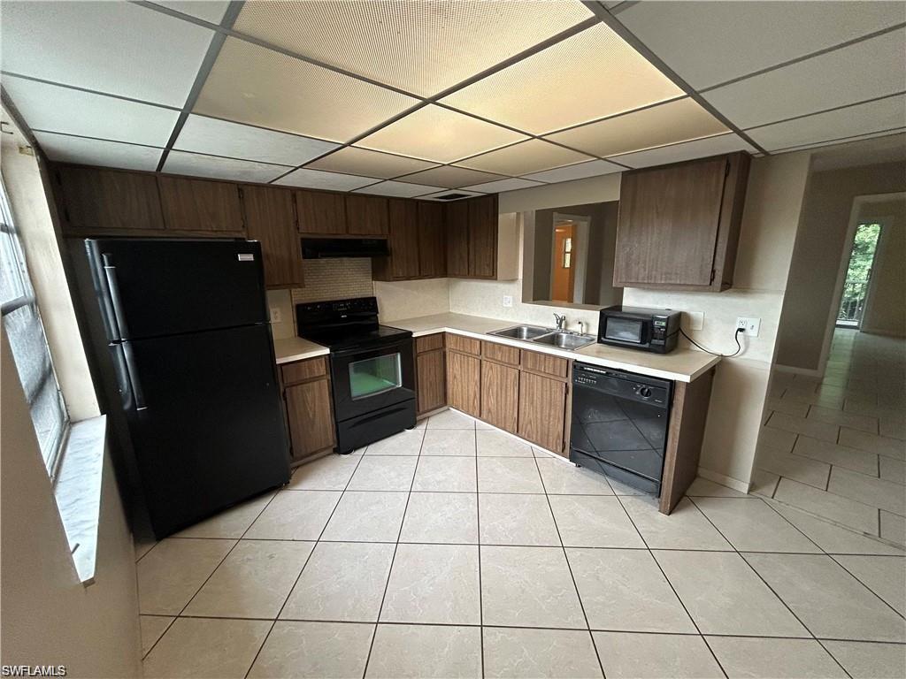 Kitchen with black appliances, light countertops, a drop ceiling, and light tile patterned floors