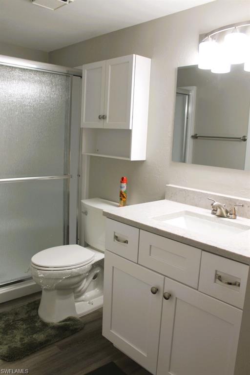 Bathroom featuring a stall shower, vanity, dark wood finished floors, baseboard heating, and a textured wall