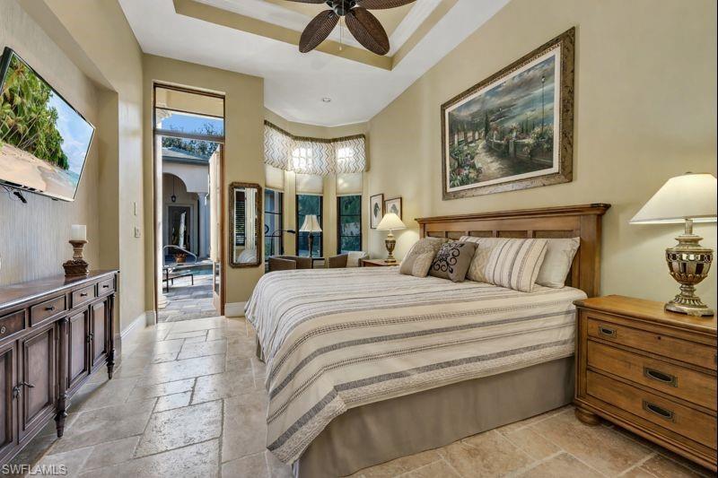 Bedroom featuring stone tile flooring, a raised ceiling, arched walkways, and ceiling fan