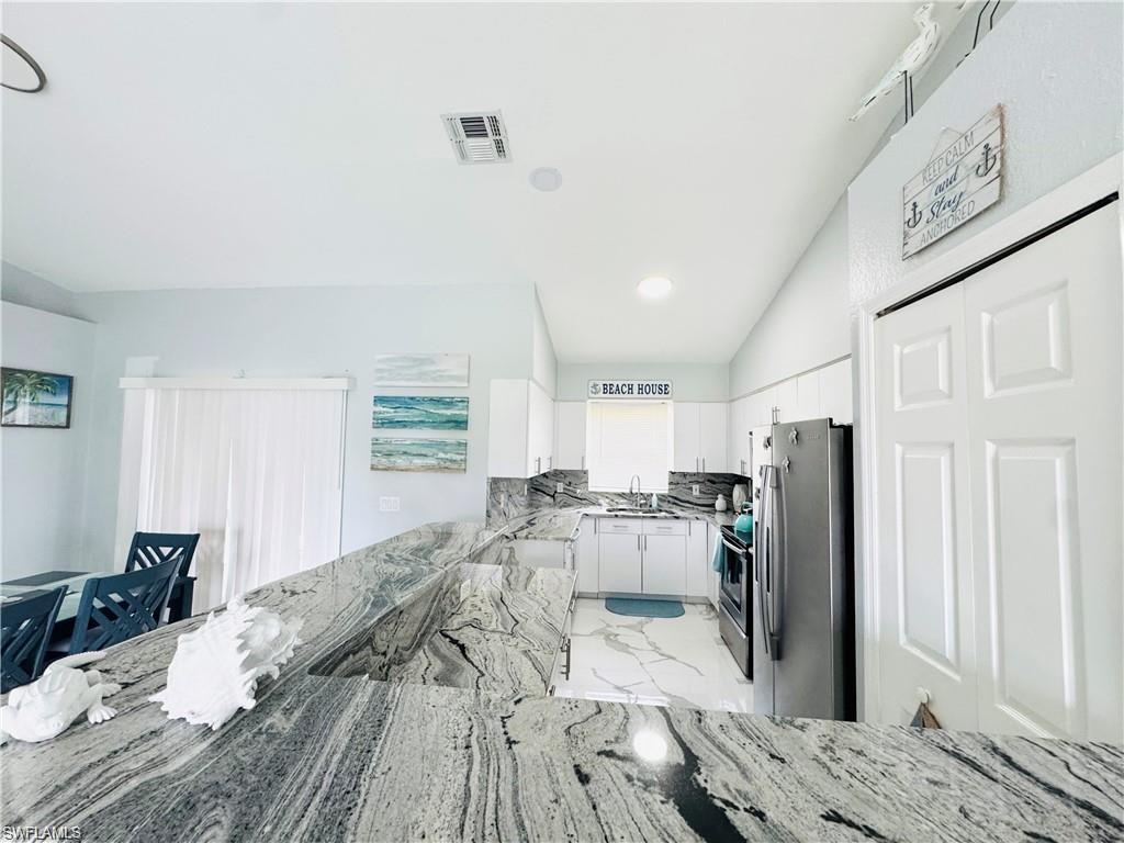 Kitchen with stainless steel appliances, white cabinetry, light marble finish flooring, light stone counters, and lofted ceiling