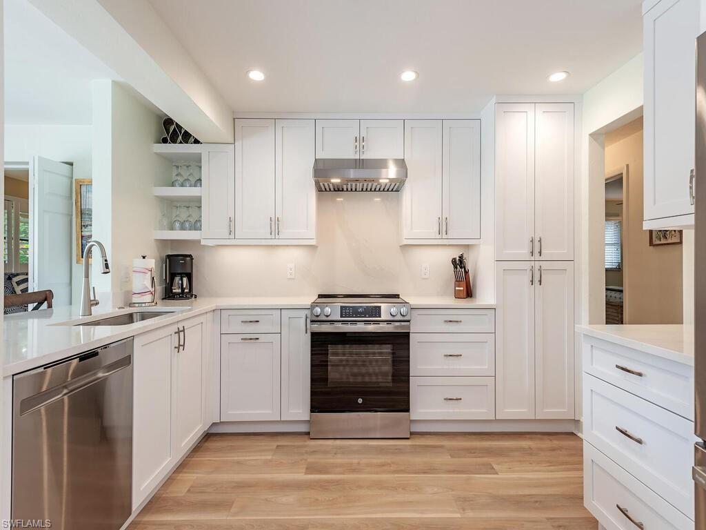 Kitchen featuring open shelves, under cabinet range hood, white cabinets, a sink, and stainless steel appliances