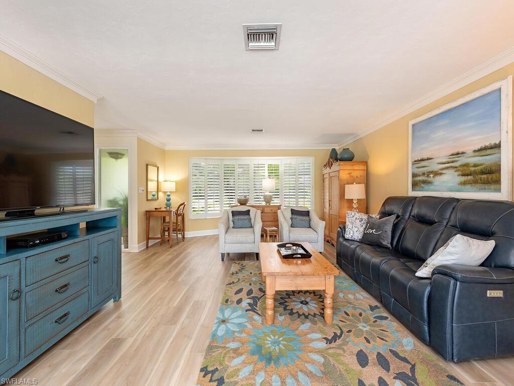 Living room with crown molding, baseboards, visible vents, and light wood-style flooring