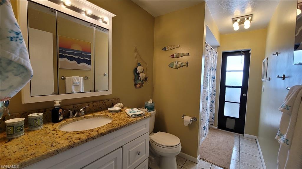 Full bathroom featuring toilet, vanity, a shower with curtain, baseboards, and tile patterned floors