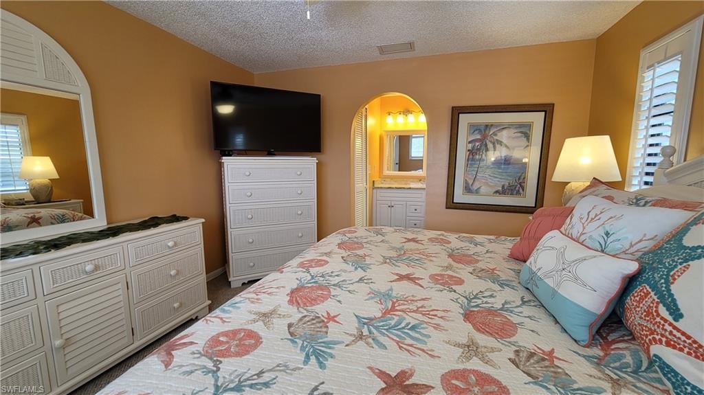Bedroom featuring a textured ceiling, multiple windows, arched walkways, and visible vents