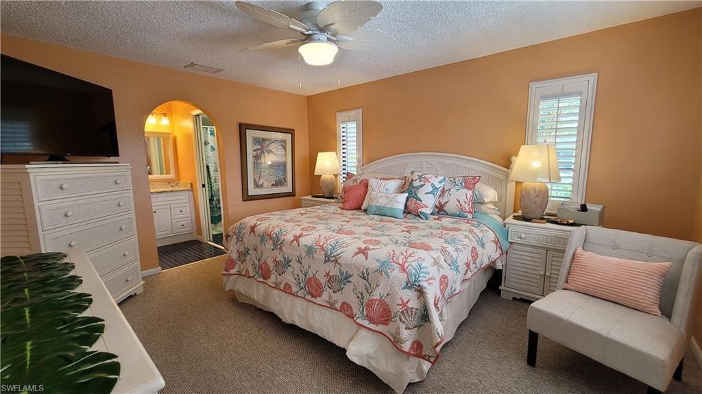 Carpeted bedroom featuring arched walkways, visible vents, a ceiling fan, a textured ceiling, and ensuite bath