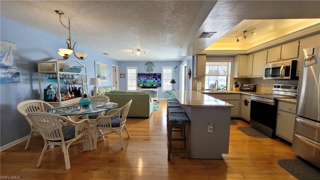 Kitchen with visible vents, decorative backsplash, open floor plan, stainless steel appliances, and light wood-type flooring