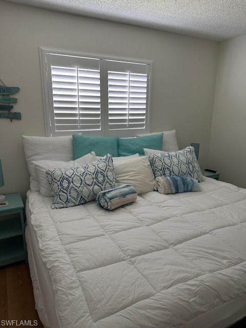 Bedroom with a textured ceiling, multiple windows, and wood finished floors
