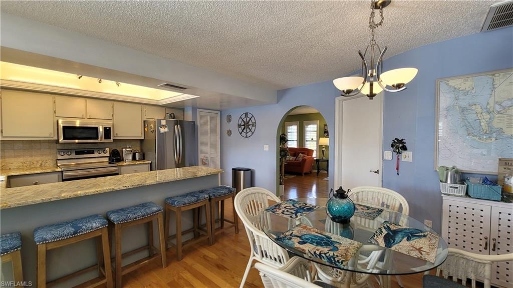 Dining area featuring arched walkways, a chandelier, visible vents, and light wood-style floors