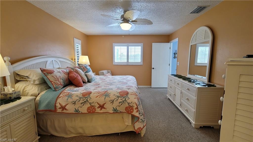 Carpeted bedroom featuring a textured ceiling, visible vents, and a ceiling fan