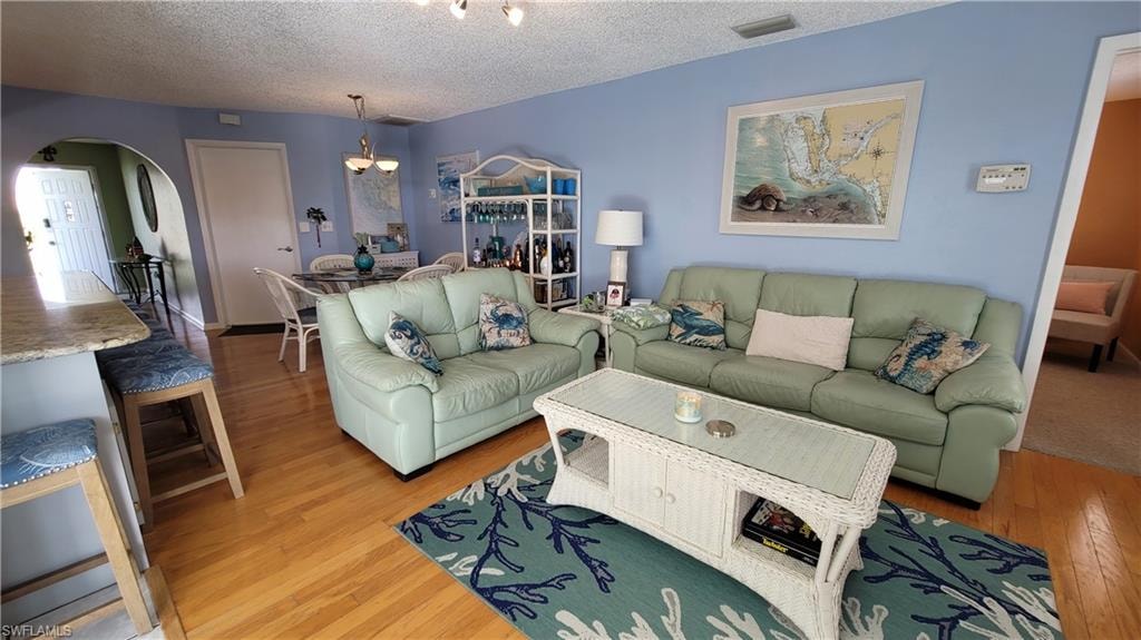 Living room with light wood-style flooring, visible vents, arched walkways, and a textured ceiling