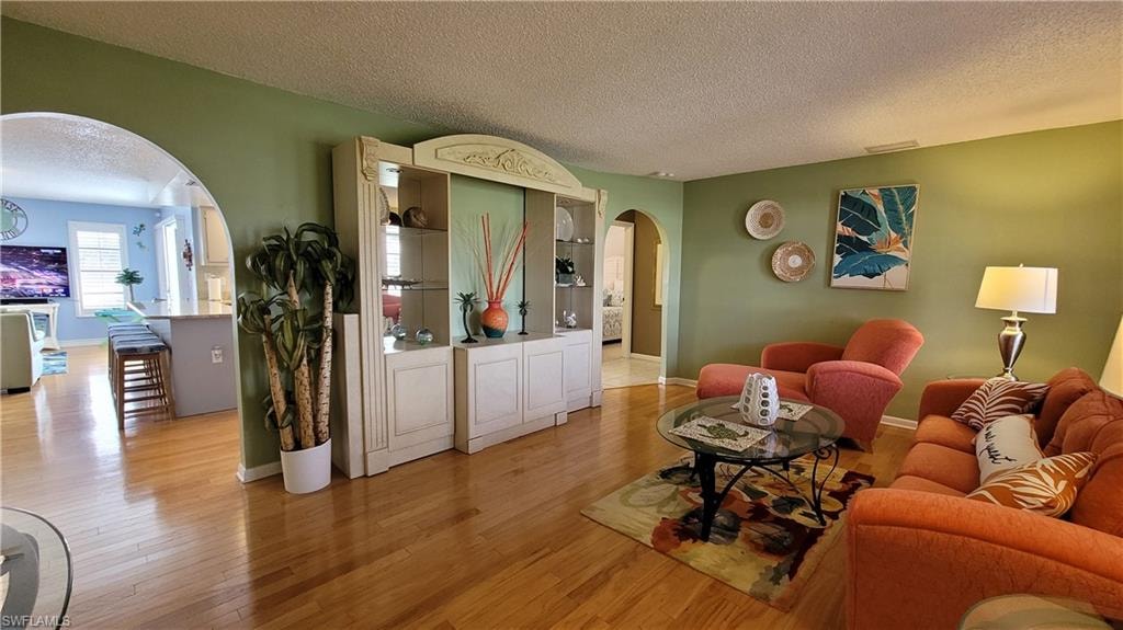 Living room with arched walkways, a textured ceiling, visible vents, baseboards, and light wood-style floors