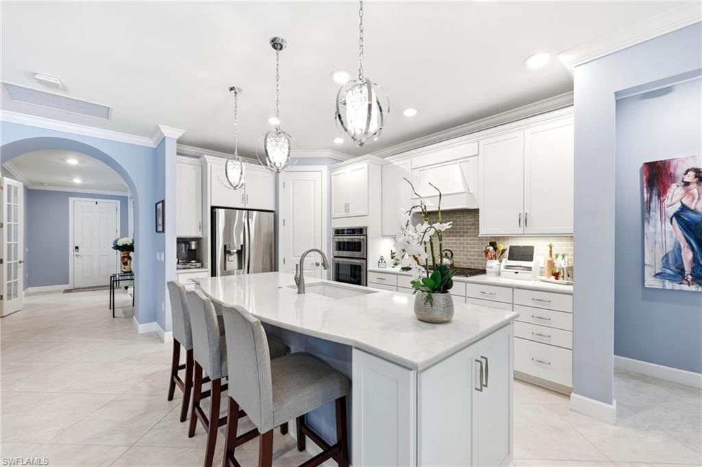Kitchen featuring white cabinets, a breakfast bar, arched walkways, an island with sink, and stainless steel appliances
