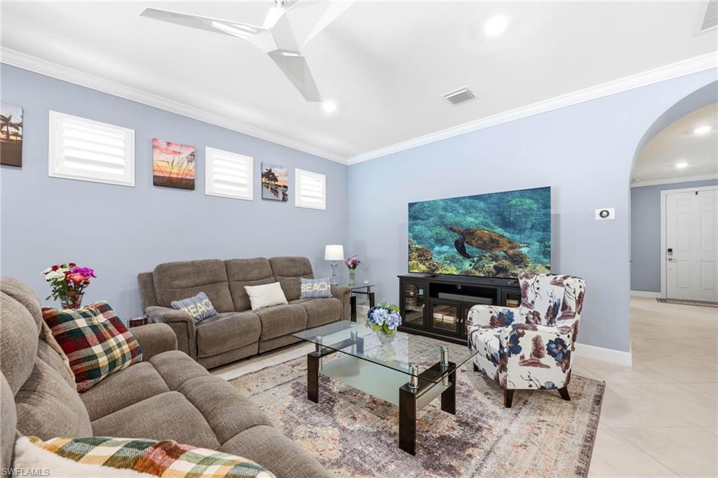 Living room with arched walkways, crown molding, tile patterned floors, a ceiling fan, and healthy amount of natural light