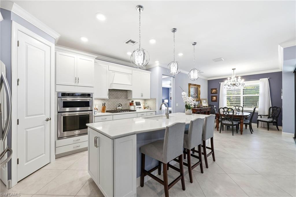 Kitchen with white cabinets, a kitchen breakfast bar, ornamental molding, a chandelier, and an island with sink