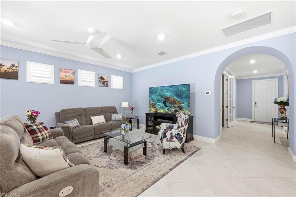 Living room with arched walkways, ornamental molding, ceiling fan, light tile patterned floors, and recessed lighting