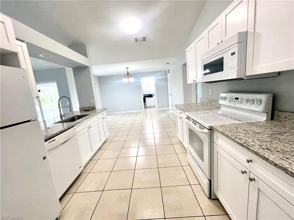 Kitchen featuring white appliances, light stone countertops, white cabinets, light tile patterned flooring, and a chandelier