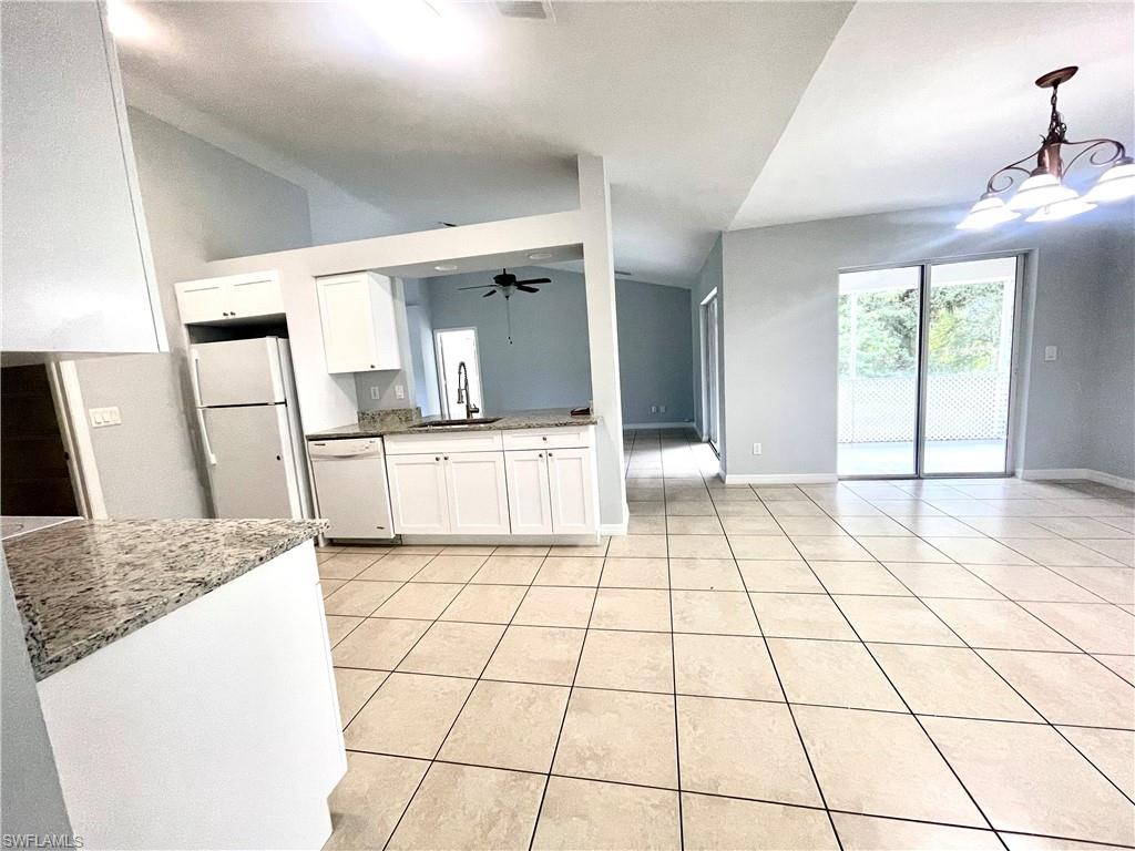 Kitchen with white cabinetry, light stone counters, vaulted ceiling, white appliances, and open floor plan