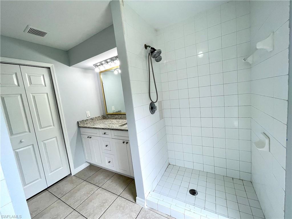 Bathroom featuring a tile shower, vanity, and light tile patterned floors