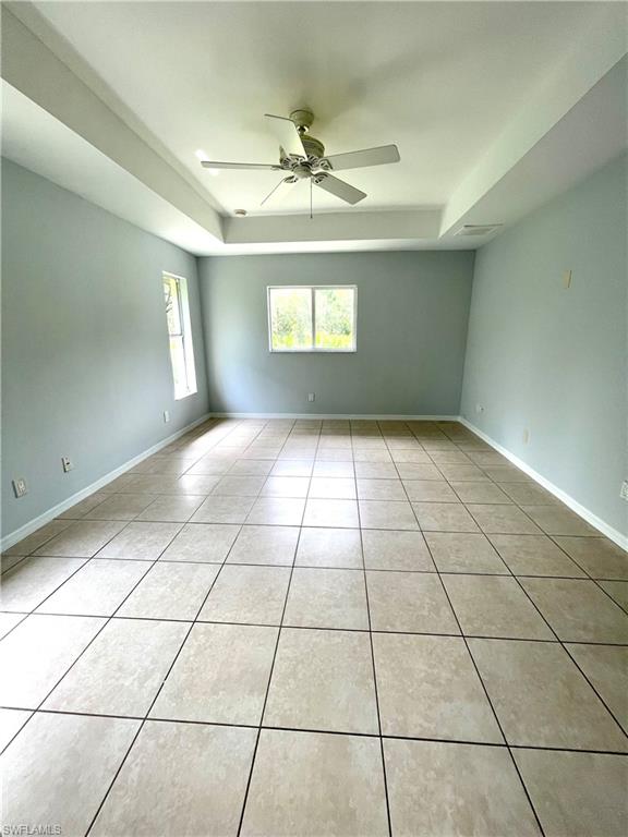 Empty room with a tray ceiling, light tile patterned floors, and a ceiling fan