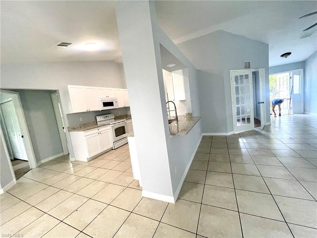Kitchen with vaulted ceiling, white appliances, white cabinets, light tile patterned floors, and light stone countertops
