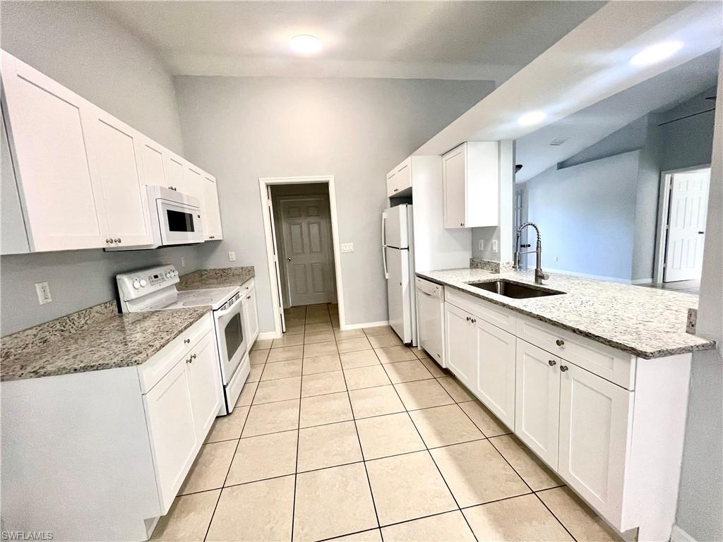 Kitchen with light stone countertops, white appliances, white cabinets, lofted ceiling, and light tile patterned floors
