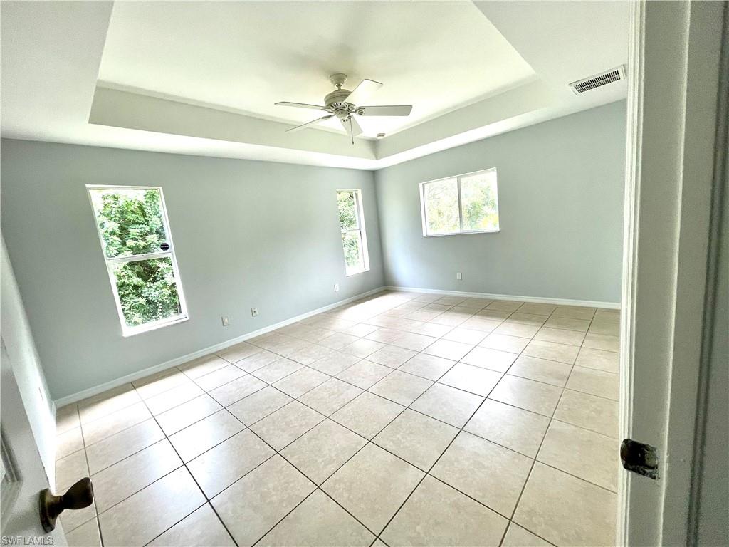 Empty room featuring a tray ceiling, light tile patterned floors, plenty of natural light, and ceiling fan
