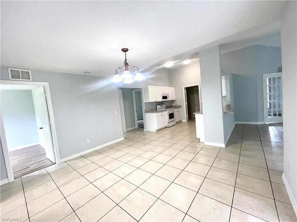 Unfurnished living room featuring a chandelier, light tile patterned floors, and lofted ceiling