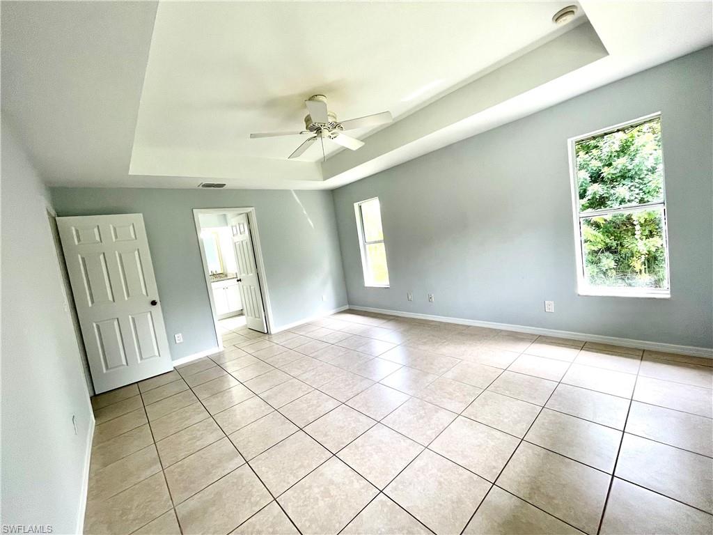 Empty room with a raised ceiling, light tile patterned floors, and ceiling fan