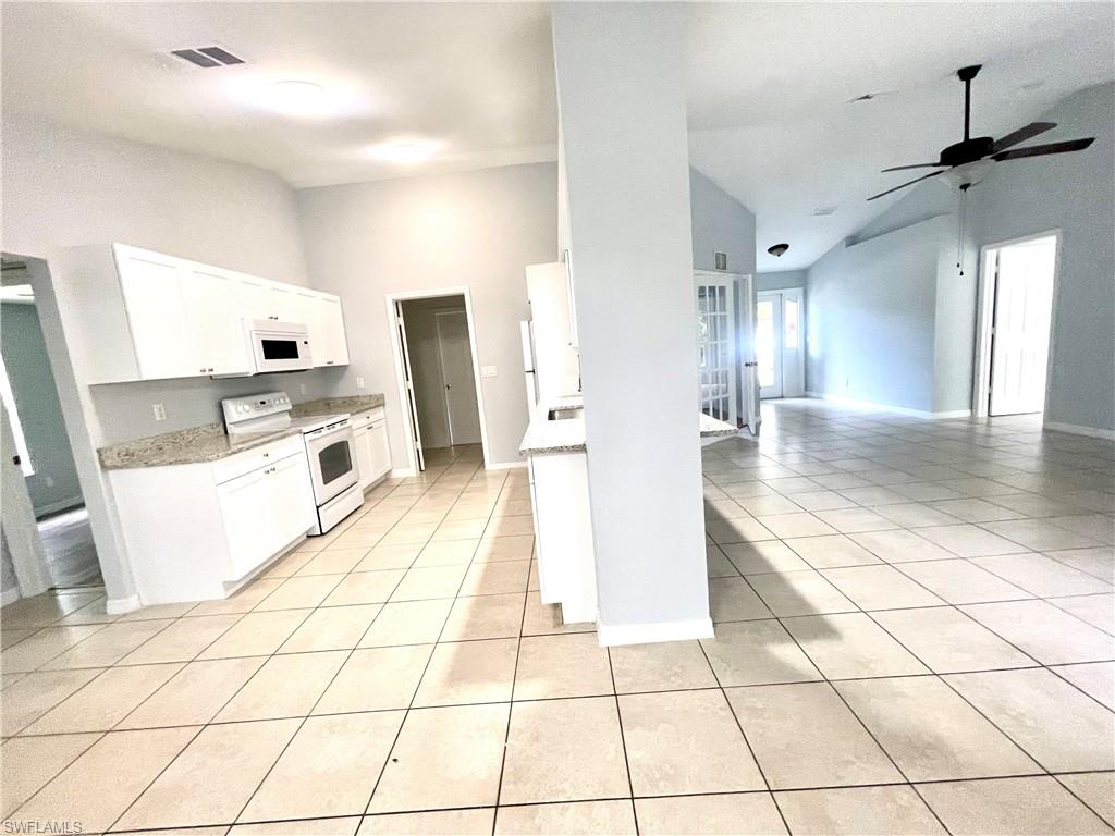 Kitchen with white appliances, white cabinets, lofted ceiling, light tile patterned floors, and ceiling fan