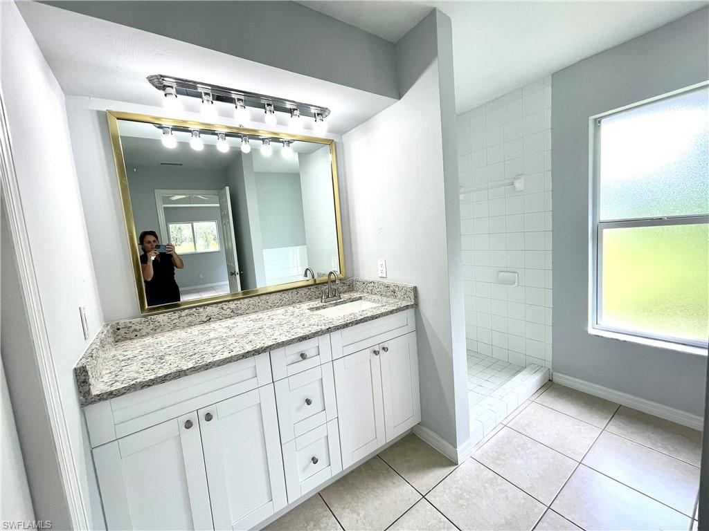 Bathroom with vanity, a tile shower, and light tile patterned floors