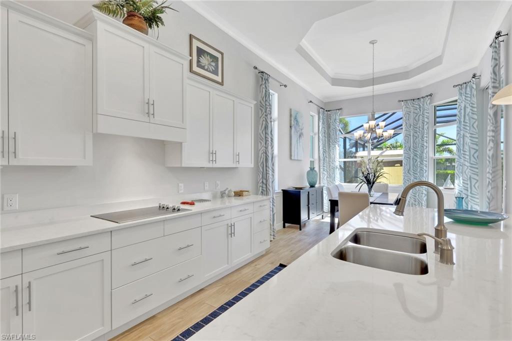Kitchen featuring white cabinetry, a raised ceiling, light stone counters, light wood-type flooring, and ornamental molding