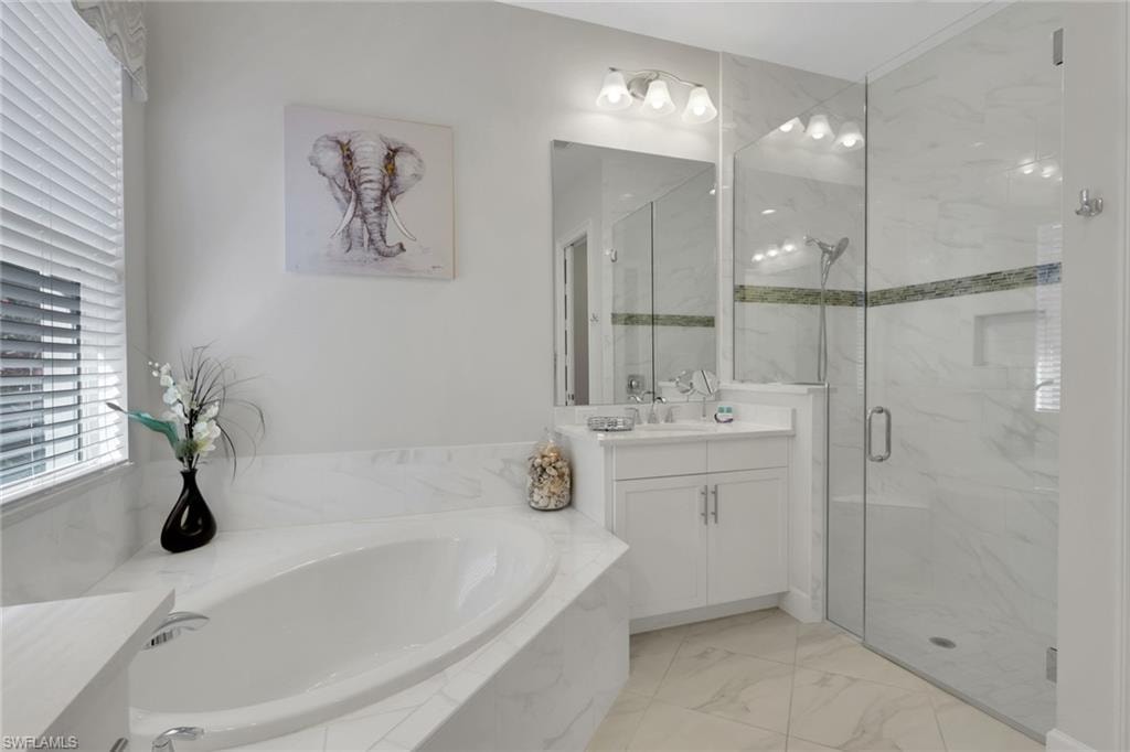 Bathroom featuring vanity, a bath, a marble finish shower, and light marble finish floors