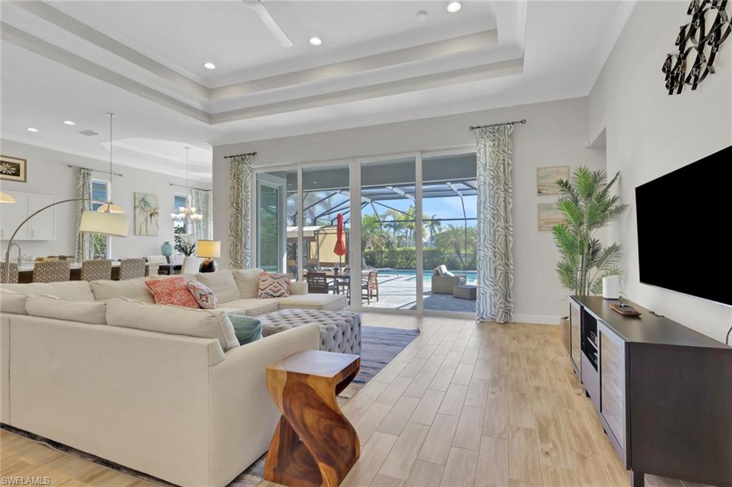 Living room with light wood-type flooring, healthy amount of natural light, a tray ceiling, a sunroom, and suspended lighting