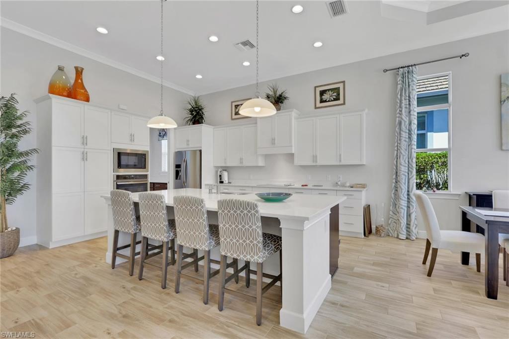 Kitchen with a kitchen bar, light wood finished floors, an island with sink, pendant lighting, and white cabinets