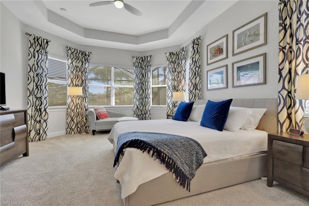 Carpeted bedroom featuring a tray ceiling and a ceiling fan