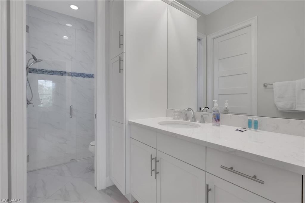 Bathroom featuring vanity, a marble finish shower, and light marble finish floors