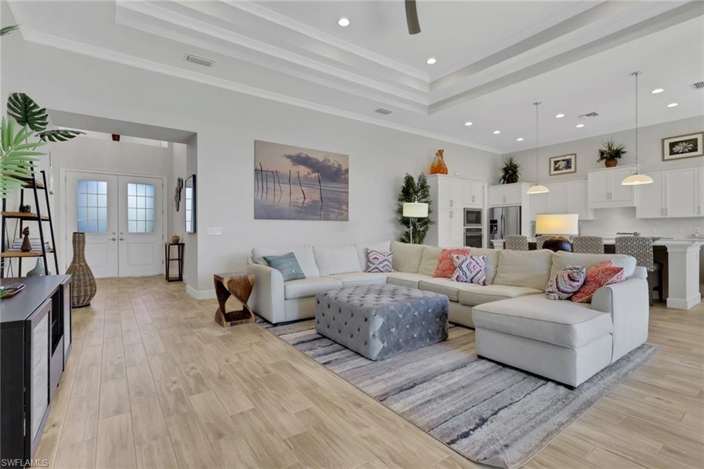 Living area with light wood-type flooring, crown molding, recessed lighting, french doors, and a tray ceiling