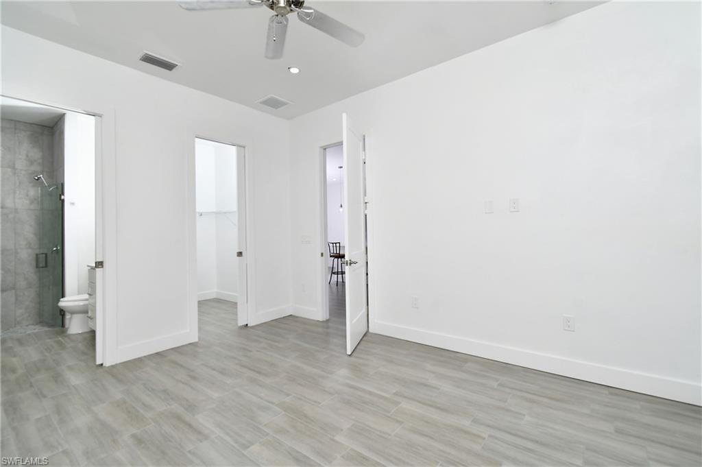 Unfurnished bedroom featuring a spacious closet, a ceiling fan, connected bathroom, and light wood finished floors