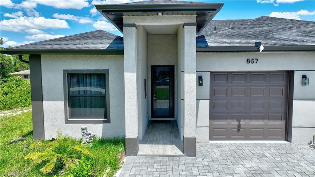 View of exterior entry featuring roof with shingles, stucco siding, a garage, and driveway