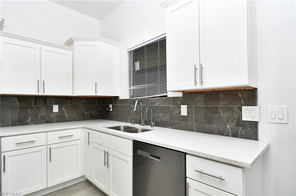 Kitchen featuring dishwasher, white cabinetry, light stone counters, and tasteful backsplash
