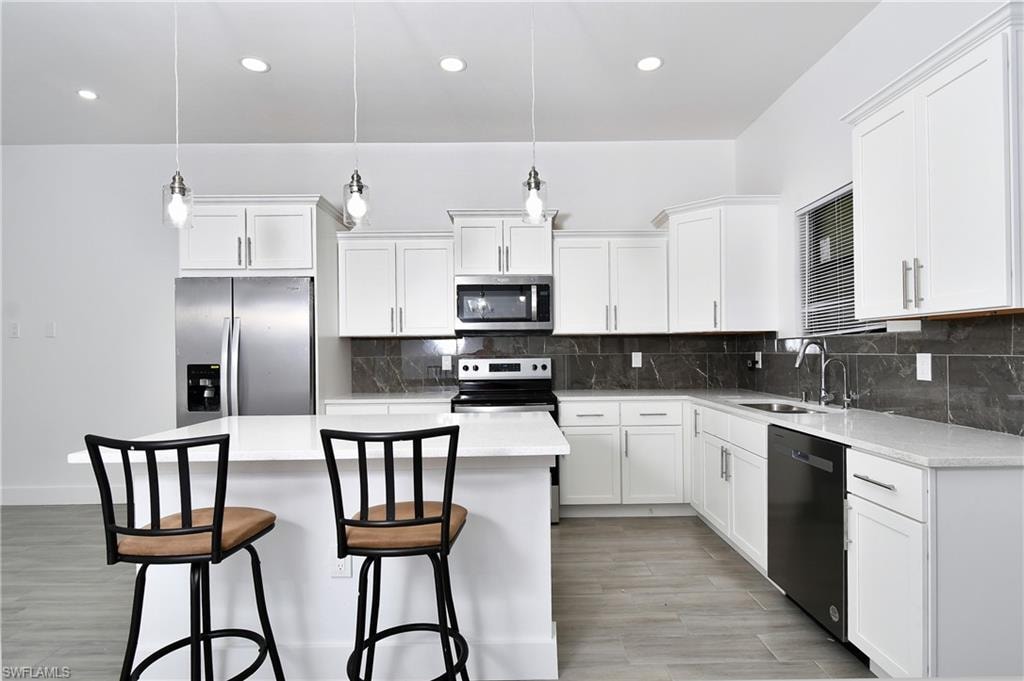 Kitchen with stainless steel appliances, pendant lighting, white cabinetry, and light wood-style floors