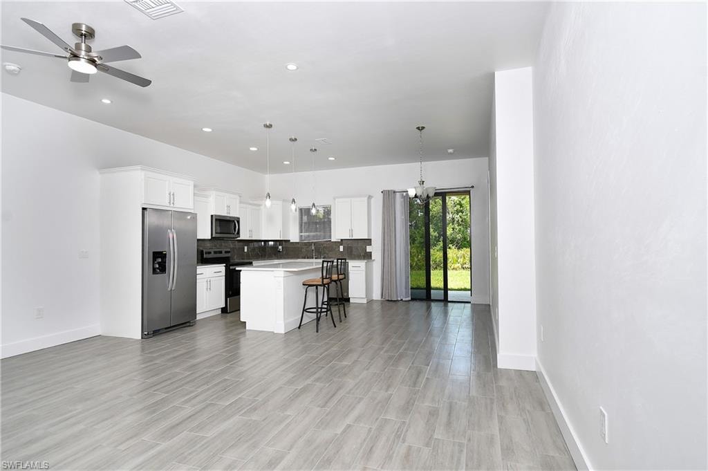 Kitchen with stainless steel appliances, a breakfast bar, white cabinetry, suspended lighting, and a kitchen island