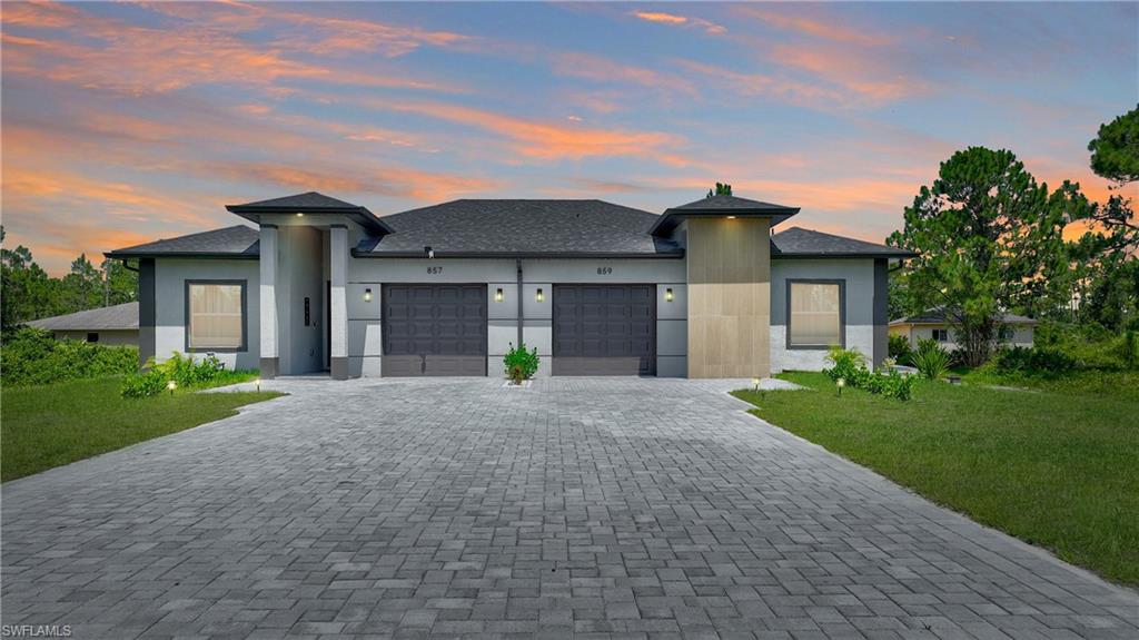 Prairie-style house featuring a front lawn, stucco siding, decorative driveway, and a garage